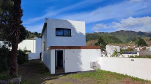 A modern white building with a small window and an open door, surrounded by greenery and hills in the background. - Atlantic Valley - Furnas (Furnas)