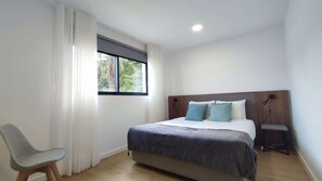 A modern bedroom with a large bed, a chair, a bedside table, and a window with a view of greenery. - Atlantic Valley - Furnas (Furnas)