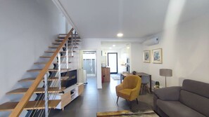 A modern living room with a wooden staircase, a yellow armchair, a grey sofa, and a flat-screen TV on a wooden stand. - Atlantic Valley - Furnas (Furnas)