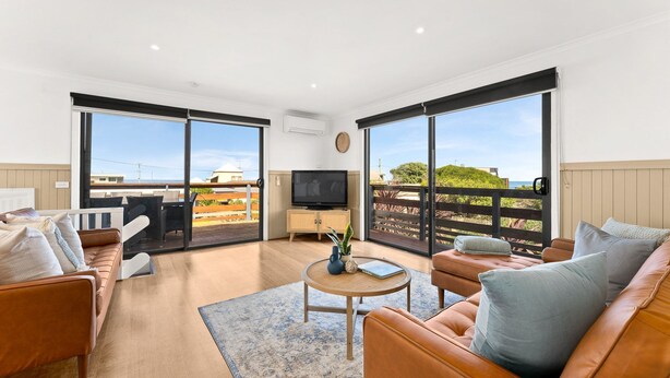 A spacious living room with a large TV, comfortable seating, and a view of the sea through expansive glass doors. - Sunderland Retreat in Sunderland Bay (Sunderland Bay)