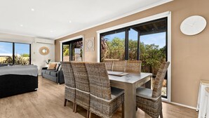 A spacious living area with a dining set and a sofa, large windows, and a view of greenery. - Sunderland Retreat in Sunderland Bay (Sunderland Bay)