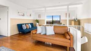 A living room with a blue sofa, a brown leather sofa, wooden flooring, and a view through a large window. - Sunderland Retreat in Sunderland Bay (Sunderland Bay)