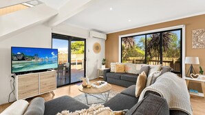 A modern living room with a television, sofa, and a view of a tropical beach through large windows. - Sunderland Retreat in Sunderland Bay (Sunderland Bay)