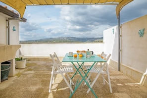 Una mesa con tetera, tazas y naranjas en una terraza con vistas a colinas distantes.