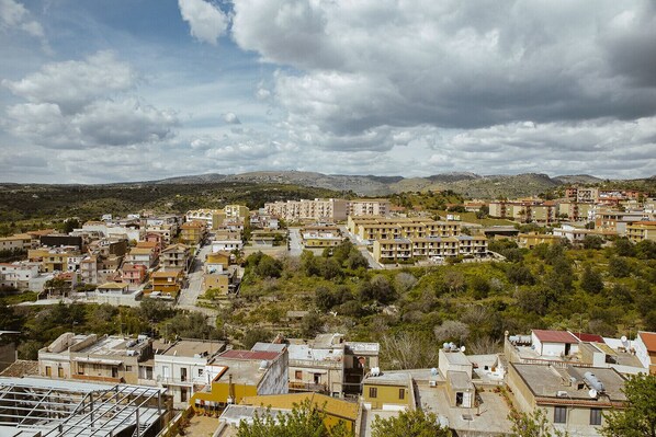 A residential area with a mix of single and multi-story buildings, surrounded by greenery and hills in the background.
