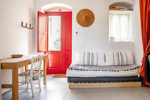Una habitación con puerta roja, cama con almohadas estampadas, mesa de madera con una cesta y un tapiz de pared tejido.