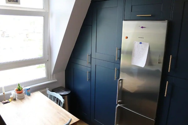 A kitchen with dark blue cabinets, a stainless steel refrigerator, and a window providing natural light.