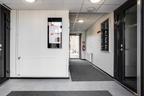 A hallway with a white wall, a bulletin board, a fire extinguisher, and a door with a sign. - Hiisi Homes Nokia (Nokia)