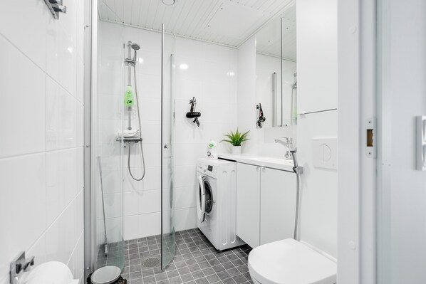 A modern bathroom with a glass-enclosed shower, a washing machine, a toilet, and a sink with a mirror. - Hiisi Homes Nokia (Nokia)