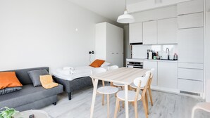 A modern living room with a grey sofa, a wooden dining table with chairs, a grey couch, and a white kitchen area with cabinets and a countertop. - Hiisi Homes Nokia (Nokia)