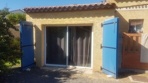 Une maison avec une porte-fenêtre coulissante, un portail bleu et une petite construction en bois.