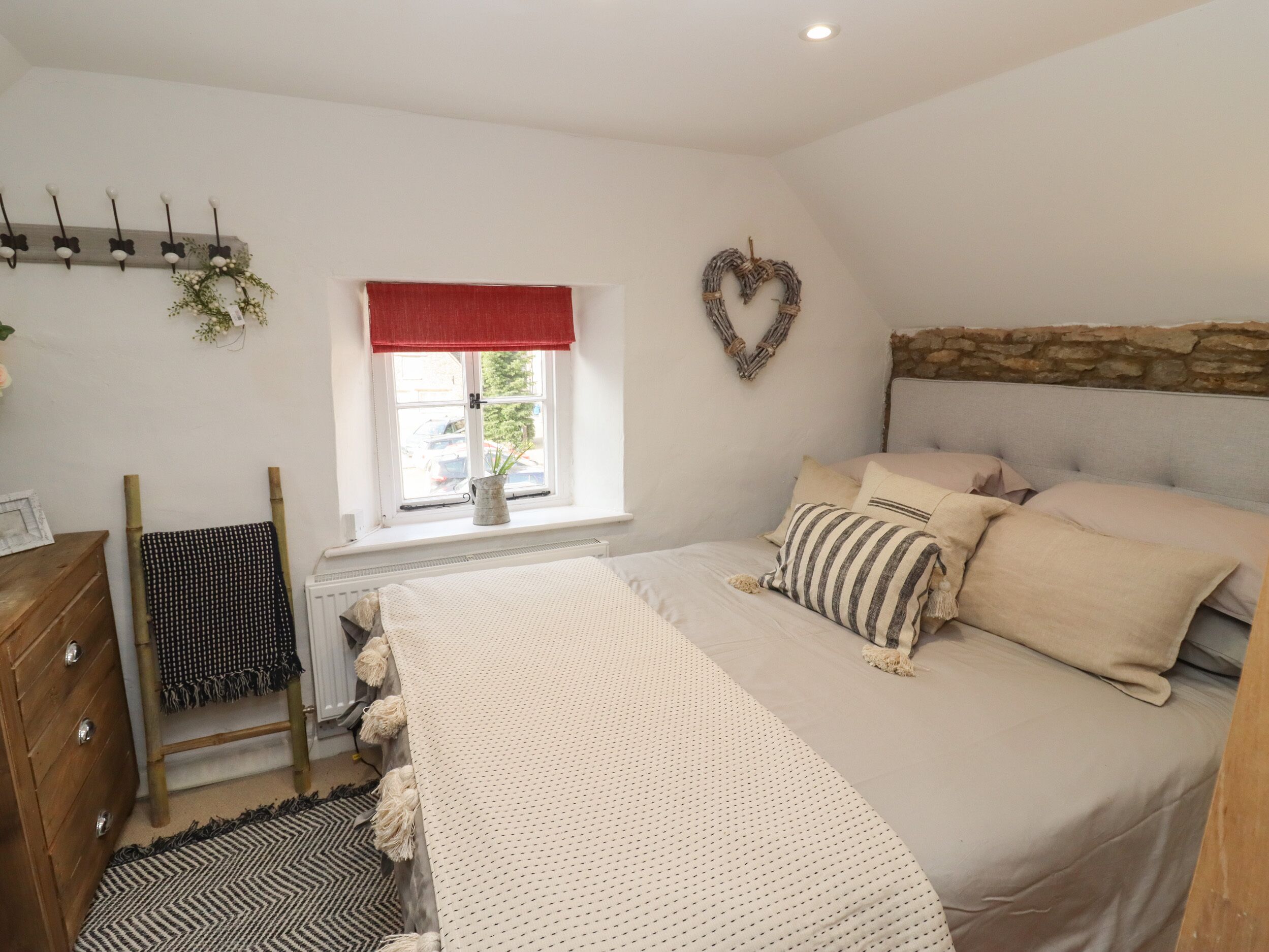 A bedroom with a bed, a dresser, a window with a view, a heart-shaped decoration, and a wall-mounted coat rack.