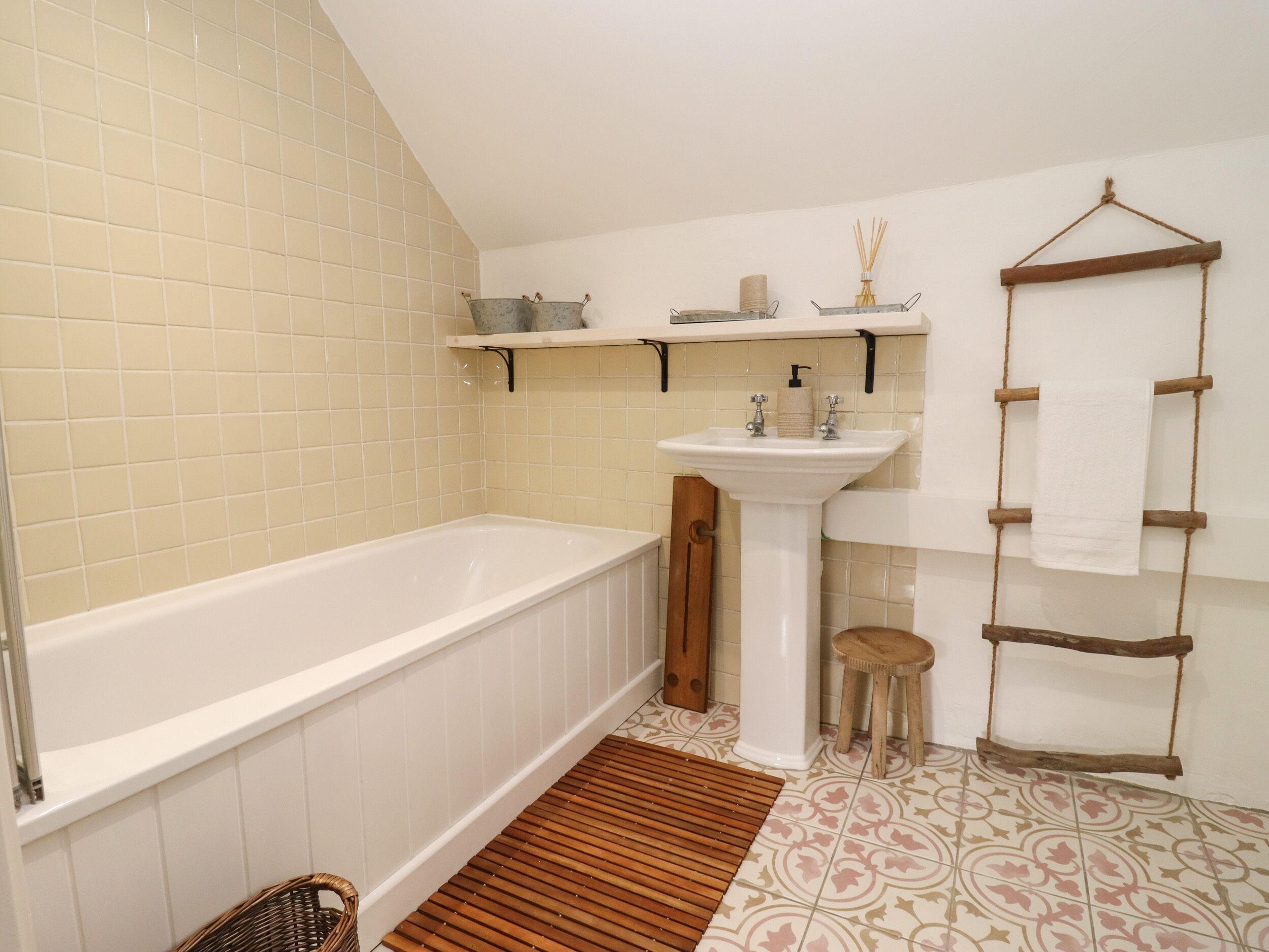 A bathroom with a bathtub, a sink, and a wooden stool. There are shelves above the sink and a towel rack on the wall.