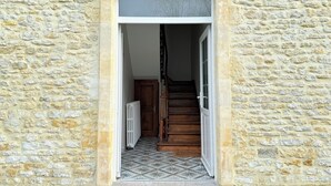 A stone building entrance with a tiled floor, a wooden door, and a staircase leading inside.