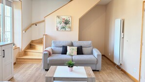 A modern living room with a grey sofa, a wooden staircase, a white radiator, and a potted plant on a coffee table.