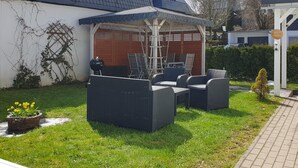A patio with outdoor furniture, a grill, and a small garden area with flowers. - Ash - Central, Indoor Playground, Garden, Switch & Stream, SummerCard (Winterberg)