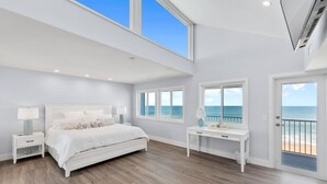 Ein geräumiges Schlafzimmer mit einem großen Bett, zwei Nachttischen, einem Schreibtisch und Meerblick durch große Fenster.