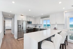 A modern kitchen with white cabinetry, stainless steel appliances, and a large island with bar seating.
