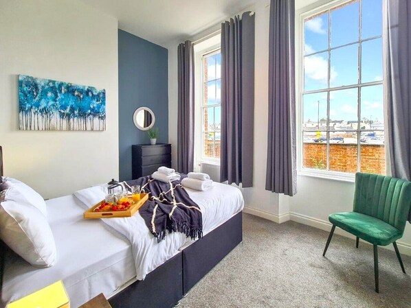 A hotel room with a bed, a green chair, a breakfast tray, a painting, and a view of the outside. - Margaret's Ground by Fortuna Property Portfolio, The Margaret's Ground (Cheltenham)