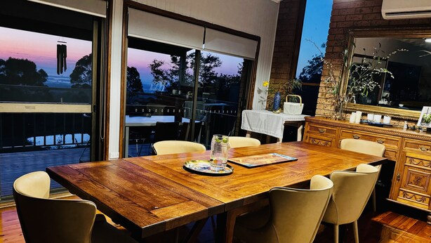 A dining area with a wooden table and chairs, a view of the outdoors, and a brick wall with a mirror and decorative items. - Idyllic Family Getaway on a farm  - Blue Mountain (Bowen Mountain)