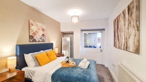 A bedroom with a bed, bedside table, and a window. - Margaret's Garden by Fortuna Property Portfolio, The Margaret's Garden (Cheltenham)