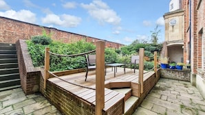 A wooden deck with seating, brick walls, and a staircase. - Margaret's Garden by Fortuna Property Portfolio, The Margaret's Garden (Cheltenham)
