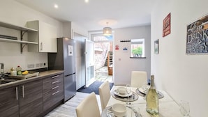 A modern kitchen with dark wood cabinets, a built-in refrigerator, and a dining area with a marble table set for four. - Margaret's Garden by Fortuna Property Portfolio, The Margaret's Garden (Cheltenham)