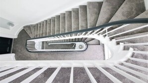 Uma escadaria em espiral com degraus revestidos de carpete e corrimãos brancos.