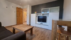 A living room with a wooden floor, a flat-screen TV, a wooden table, a dark sofa, and a wooden chair.