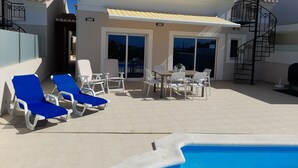 Un área junto a la piscina con sillones de descanso, una mesa de comedor y un porche cubierto.