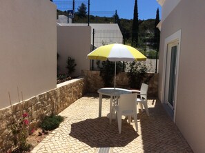 Une terrasse avec une table et des chaises, un parasol jaune et blanc, et un mur en pierre.