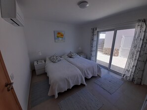 Une chambre avec deux lits, une table de chevet, une lampe, un tableau et une vue à travers une porte vitrée.