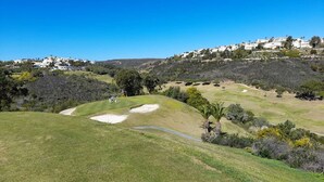 Un campo de golf con búnkeres, un sendero sinuoso y edificios residenciales al fondo.
