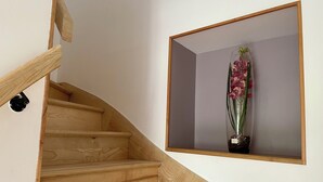 A wooden staircase with a wall-mounted shelf holding a potted orchid. - Les Pensées (Saint-Vigor-le-Grand)