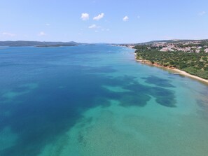 An aerial view of a coastal area with clear blue waters, a sandy beach, and a densely populated town with buildings. - Villa Primorje (Sveti Filip i Jakov)