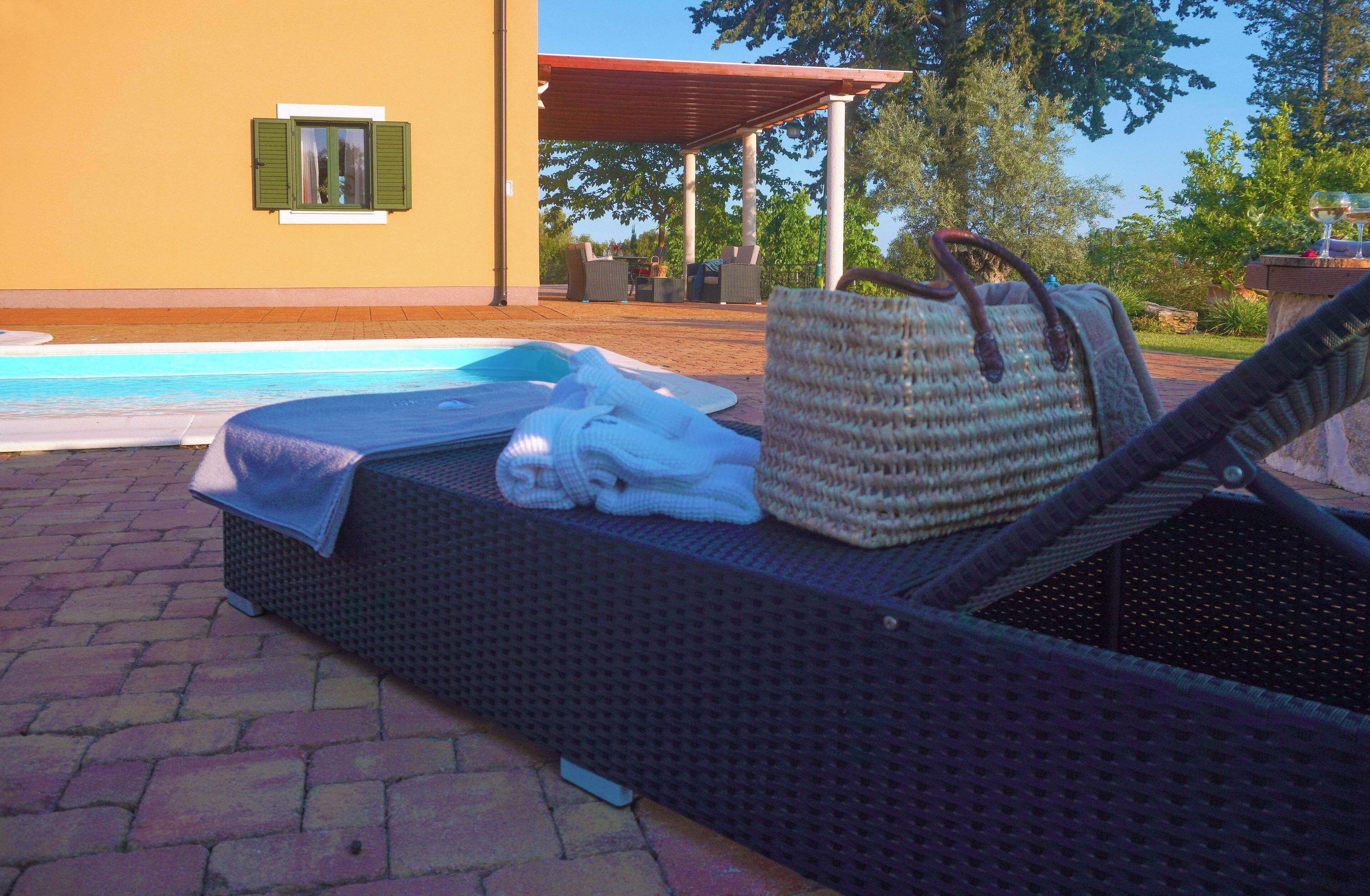 Un área de descanso junto a la piscina con una silla de mimbre, un bolso tejido y una toalla.