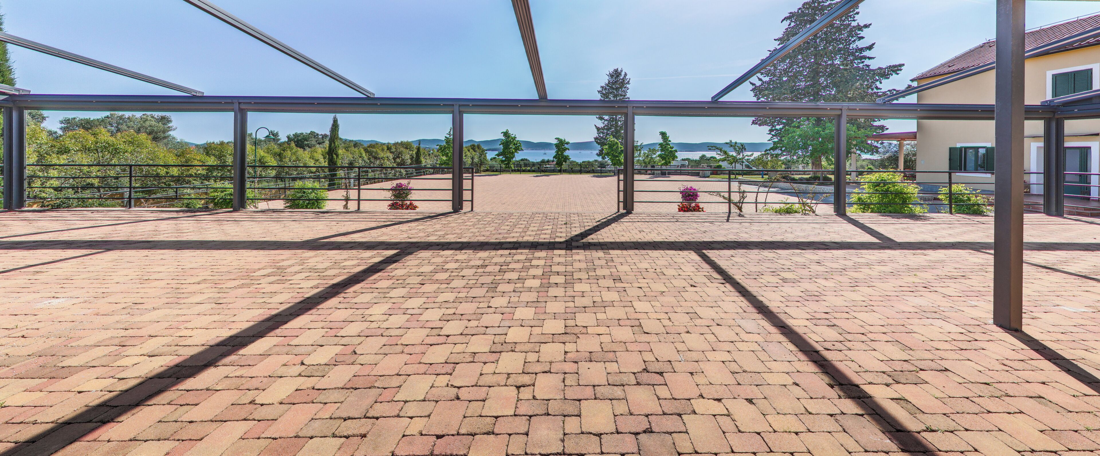 A covered outdoor area with a brick floor, metal railings, and a view of the sea and hills.