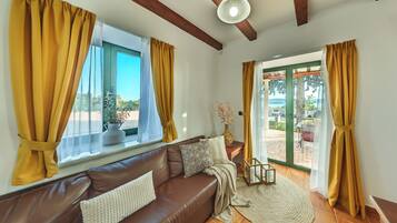 A cozy living room with a brown leather sofa, a round rug, and a view of a garden through a glass door.