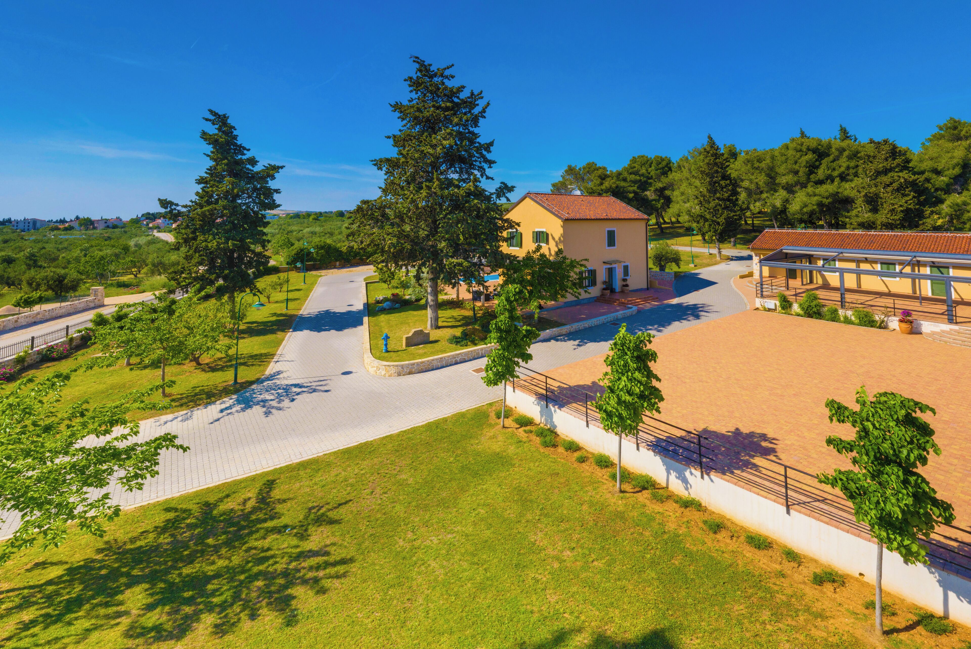 A large, open courtyard with a paved walkway, surrounded by trees and a building with a tiled roof.