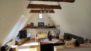 A cozy loft-style living space with a sloped ceiling, a dining area, a sofa, and a television.