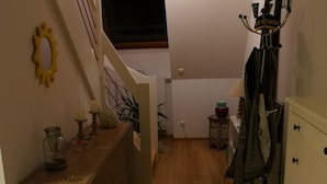 A narrow hallway with a wooden floor, a small rug, a coat rack, and a staircase leading to an upper level.