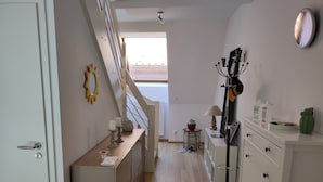A hallway with a staircase, a mirror, a coat rack, and a small table with a lamp and candles.