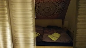 A bedroom with a bed, pillows, and a patterned tapestry on the wall.
