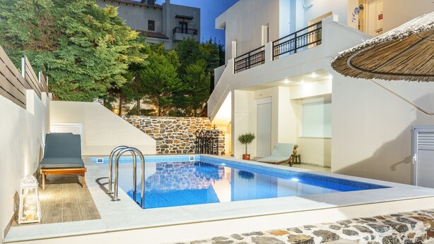 A modern pool area with a stone-tiled deck, a lounge chair, and a small table.