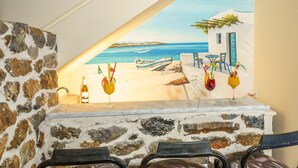 A bar area with a stone wall and a mural of a beach scene. There are three chairs and a table with drinks.