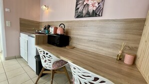 A compact kitchen with a wooden countertop, two white chairs, a microwave, a kettle, and a small cabinet. - Le Cocon - Towncenter (Bayeux)