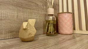 A wooden sculpture, a glass bottle with reed sticks, and a pink container on a wooden surface. - Le Cocon - Towncenter (Bayeux)