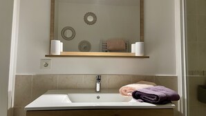 A bathroom with a white sink, a mirror above it, and a towel rack with towels. - Le Cocon - Towncenter (Bayeux)