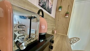 A kitchenette with a pink toaster, a kettle, and a coffee maker. There is a wooden slatted wall behind the appliances, and a small potted plant on the wall. - Le Cocon - Towncenter (Bayeux)