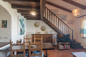 A cozy living room with a wooden staircase, a dining table with chairs, a television, and a bookshelf. - Piazzetta Casa Dora 20m From The Sea (Loiri Porto San Paolo)